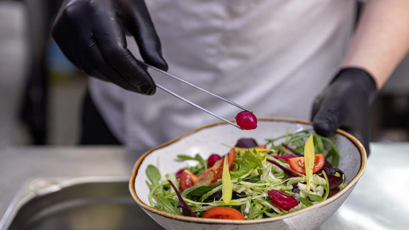 Cuisinier utilisant une pince de cuisine pour retourner des aliments dans une poêle.